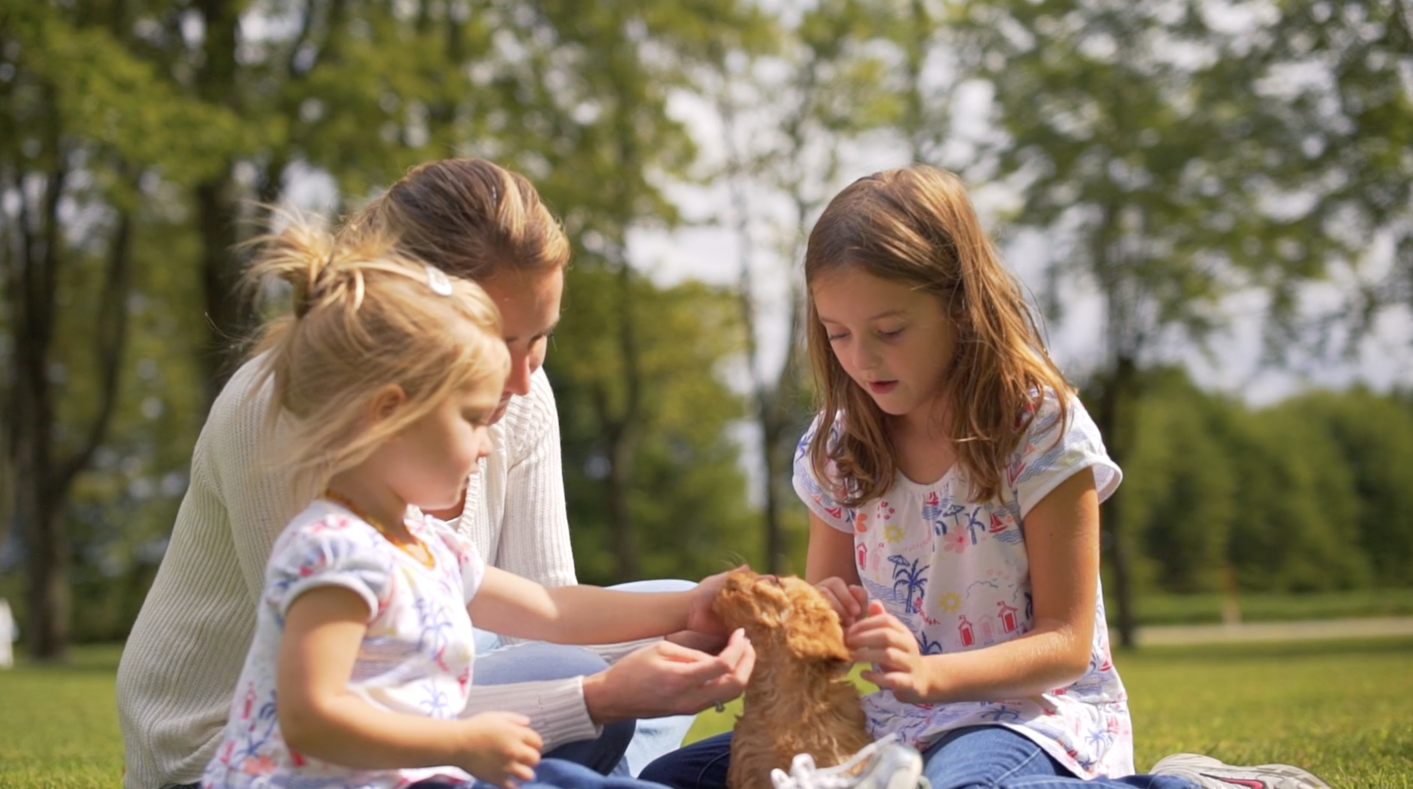 two small girls and a woman petting a puppy outdoors