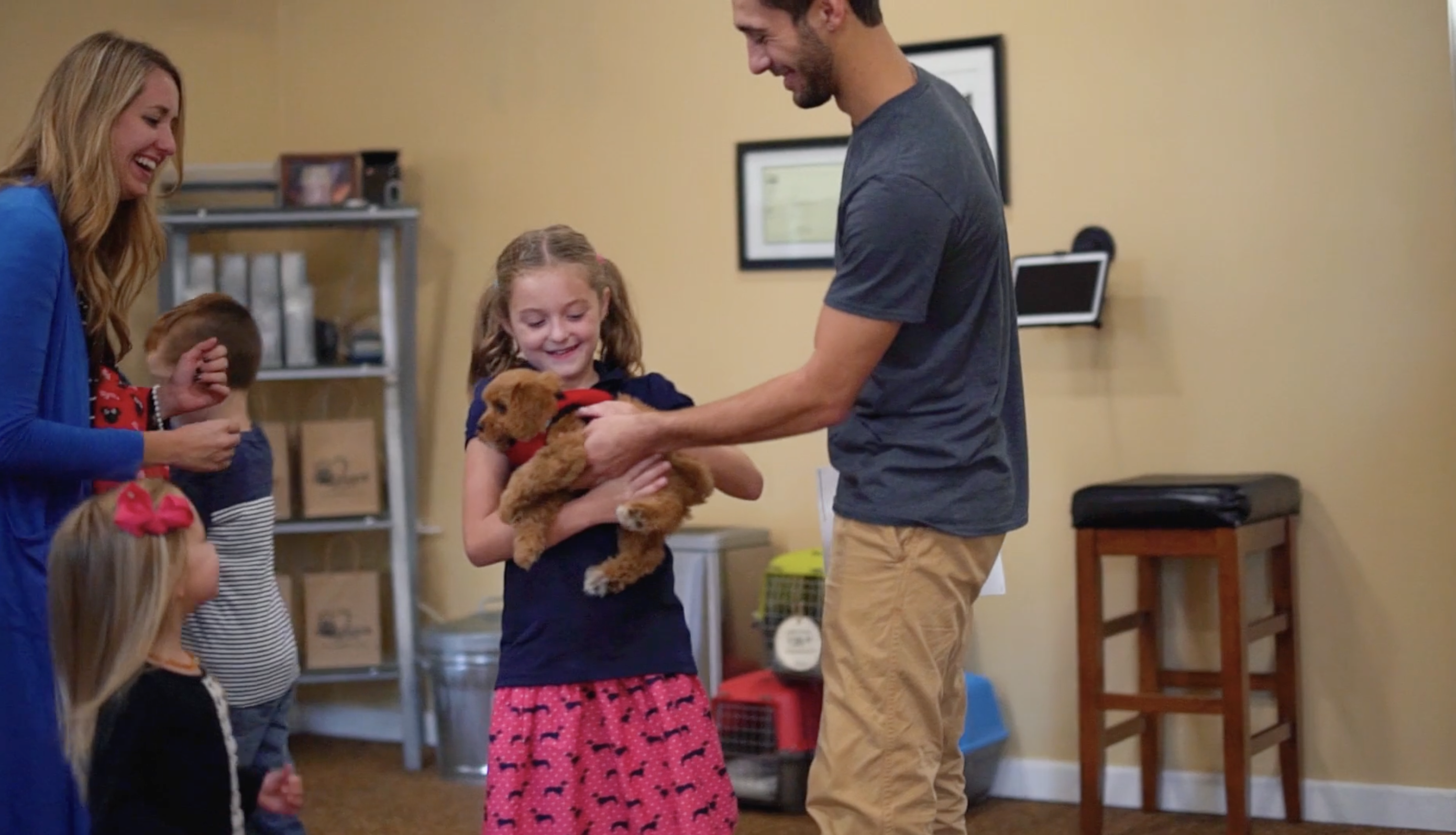 premier pups employee at premier pups handing a puppy to a mother and three children