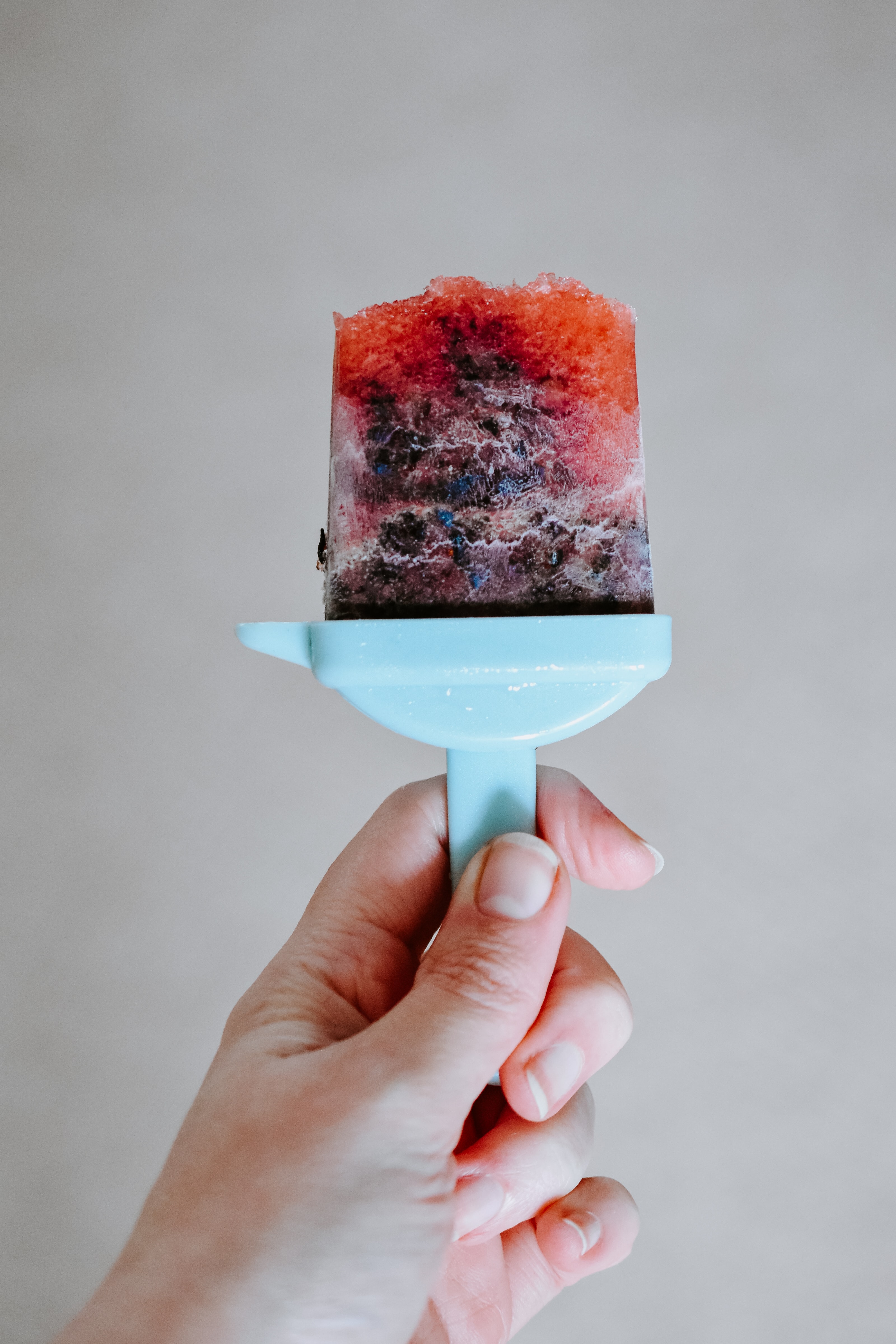 person holding a popsicle made of watermelon and blueberry