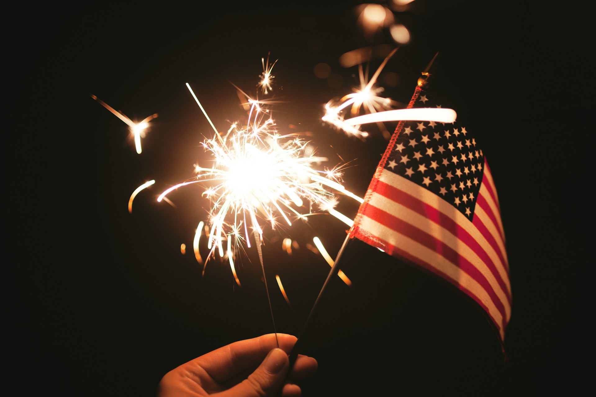 person holding an american flag and small lit firework